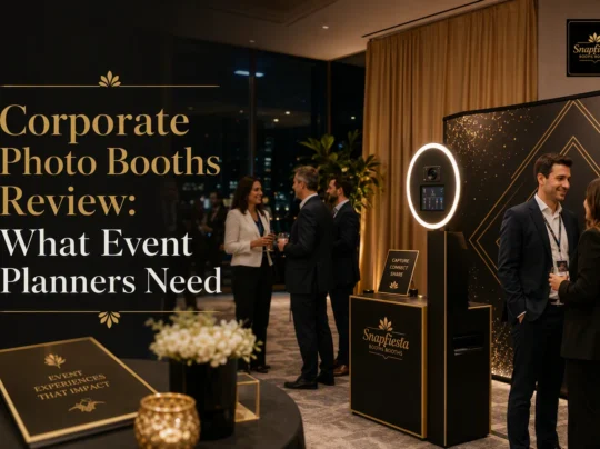 Business professionals chat near a modern photo booth at an elegant indoor event. The scene features a sign titled “Corporate Photo Booths Review: What Event Planners Need.” The atmosphere is warm and sophisticated.